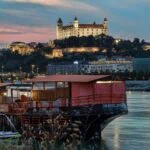 Bratislava Castle illuminated above the Danube River at sunset with boats along the Bratislava waterfront in Slovakia