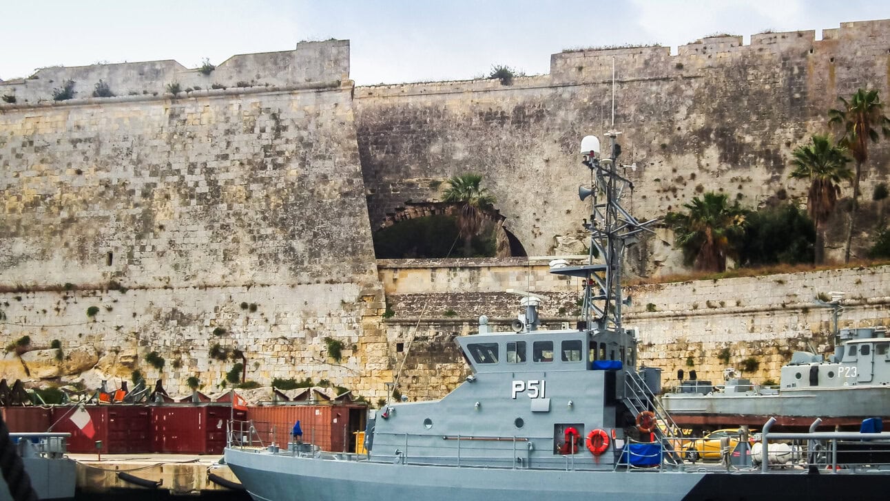 Historic fortress walls of Valletta overlooking naval vessels and harbour infrastructure in Malta