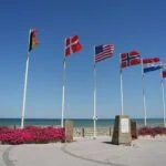 Allied nation flags flying beside a Normandy D-Day memorial overlooking the beaches in northern France