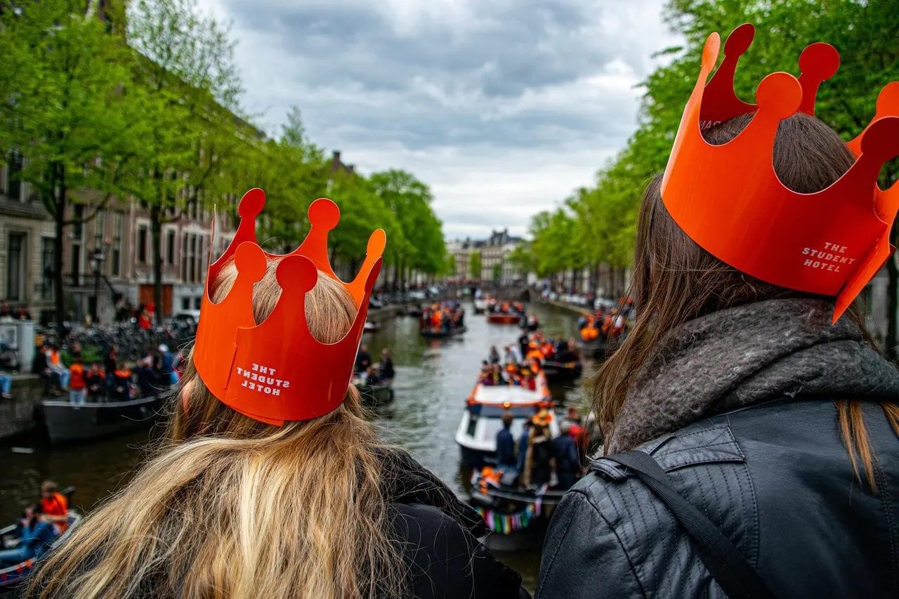Travellers wearing orange crowns overlooking crowded Amsterdam canals during King’s Day celebrations in the Netherlands