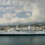 Large passenger ferry arriving into Messina Port in Sicily, with the Sicilian coastline and mountains visible behind the ship