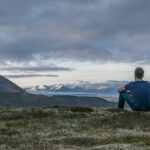 solo traveller sitting on mountain overlooking landscape and glacier view