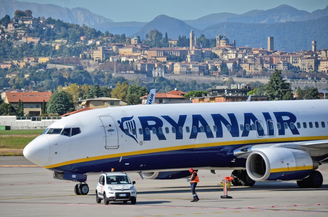 Ryanair aircraft at Milan Bergamo Airport with Bergamo's historic Città Alta and Venetian Walls visible in the background.