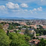 Panoramic view across Bergamo from Città Alta, showcasing the city's historic rooftops, green hills and the surrounding Lombardy countryside.