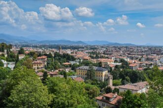 Panoramic view across Bergamo from Città Alta, showcasing the city's historic rooftops, green hills and the surrounding Lombardy countryside.