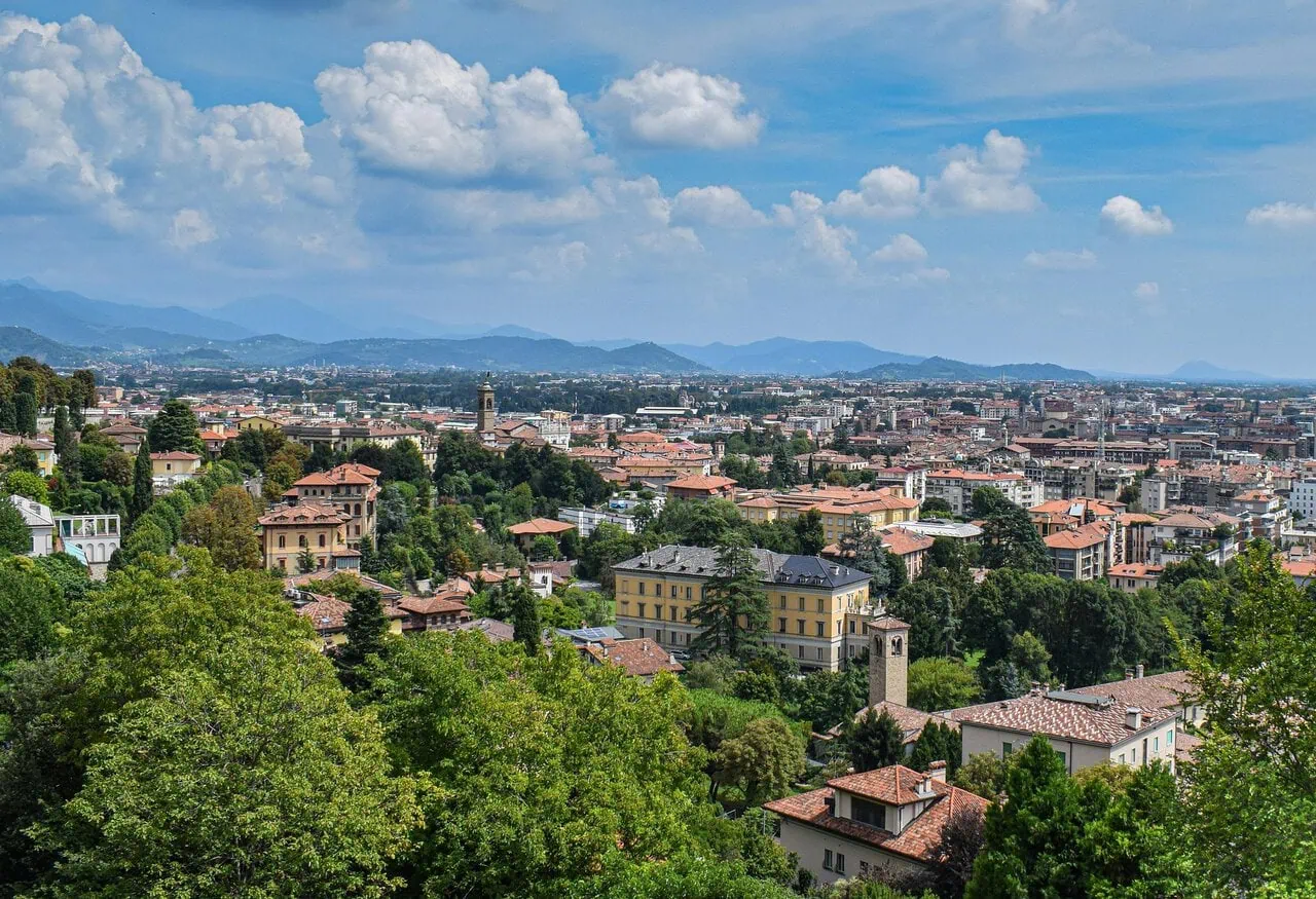 Panoramic view across Bergamo from Città Alta, showcasing the city's historic rooftops, green hills and the surrounding Lombardy countryside.