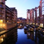 Birmingham canal district at night with illuminated apartments, narrowboats and waterside reflections.