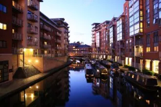 Birmingham canal district at night with illuminated apartments, narrowboats and waterside reflections.
