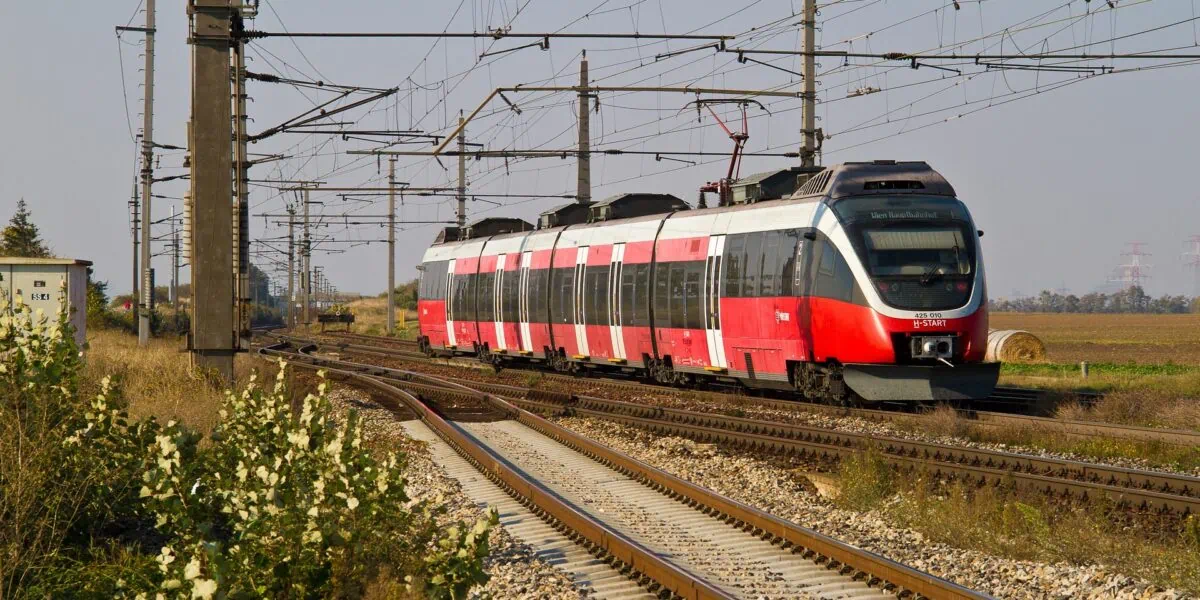 Regional train travelling through the Austrian countryside under overhead power lines.
