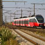 Regional train travelling through the Austrian countryside under overhead power lines.