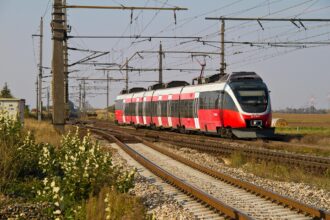 Regional train travelling through the Austrian countryside under overhead power lines.