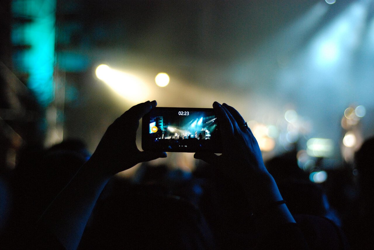 Eurovision-style concert audience recording a live performance on a smartphone.