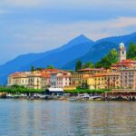 Bellagio waterfront on Lake Como with colourful buildings, ferry terminal and the Italian Alps in the background.
