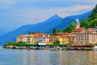 Bellagio waterfront on Lake Como with colourful buildings, ferry terminal and the Italian Alps in the background.