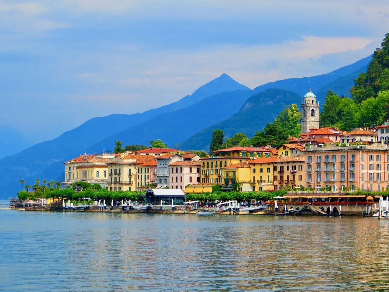 Bellagio waterfront on Lake Como with colourful buildings, ferry terminal and the Italian Alps in the background.