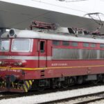 Red BDŽ electric locomotive preparing to depart from Sofia Central Railway Station on a night train service.