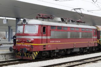 Red BDŽ electric locomotive preparing to depart from Sofia Central Railway Station on a night train service.