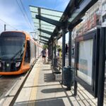 A modern orange Athens tram waiting beside a passenger platform.