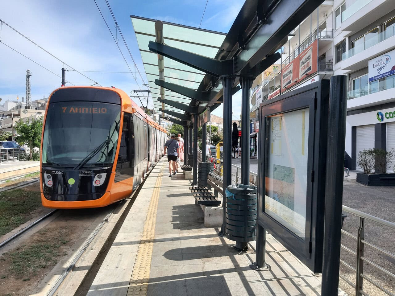 A modern orange Athens tram waiting beside a passenger platform.