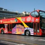 A red open-top sightseeing bus travelling through central Athens.