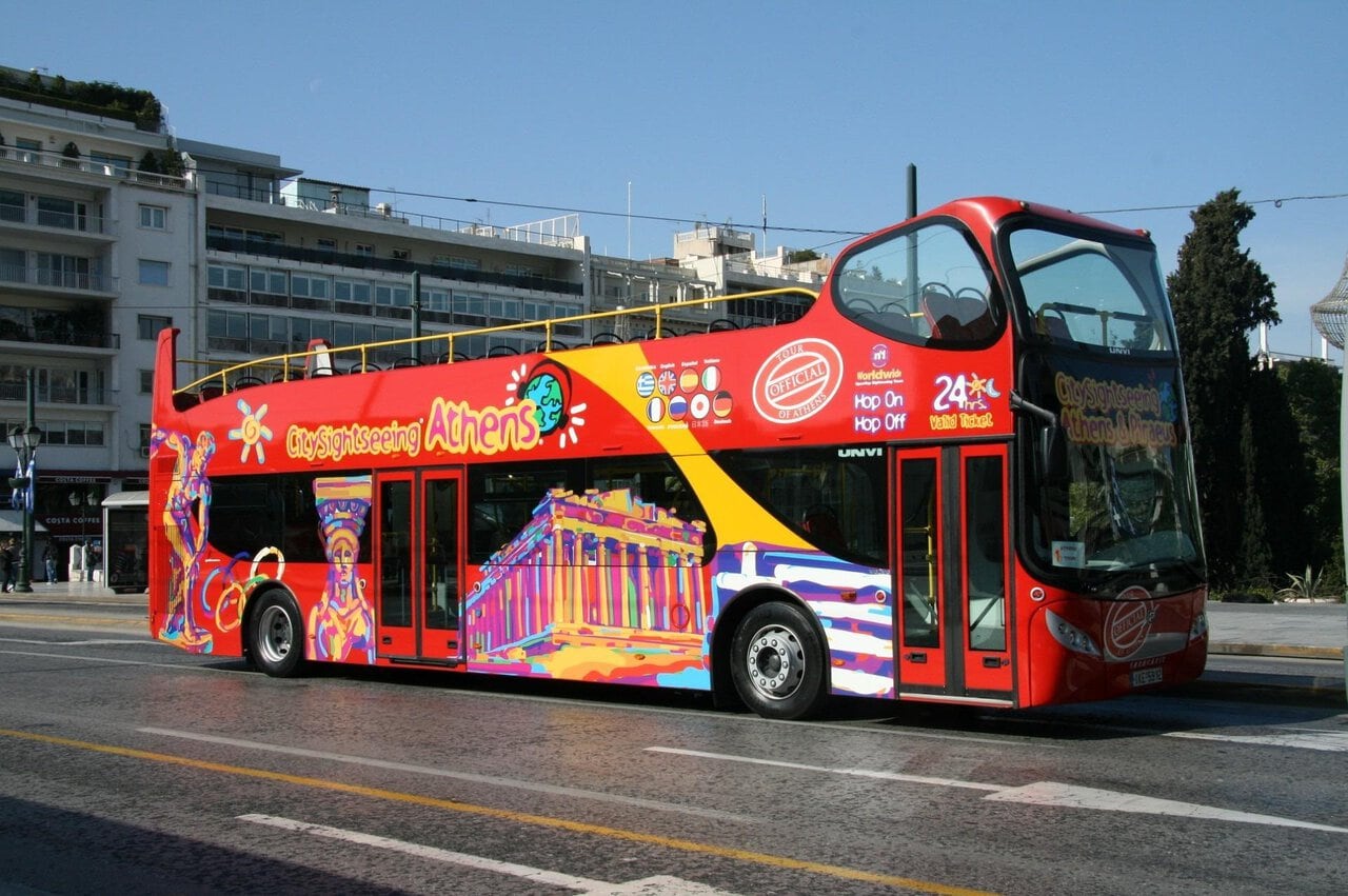 A red open-top sightseeing bus travelling through central Athens.