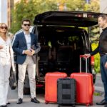 Professional chauffeur helping travellers with luggage beside a private airport transfer vehicle.