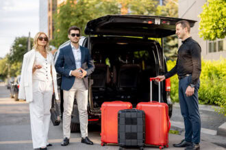 Professional chauffeur helping travellers with luggage beside a private airport transfer vehicle.
