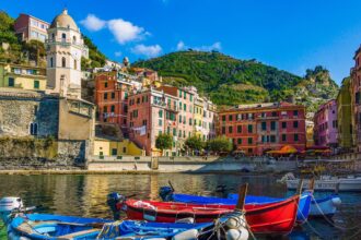 Colourful fishing boats moored in Vernazza harbour with traditional Ligurian houses behind.