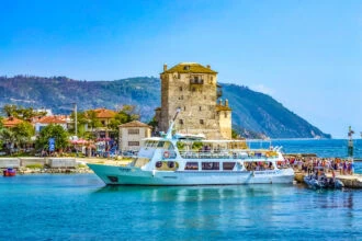 Ouranoupoli harbour with the Tower of Prosphorion and sightseeing boat in Halkidiki, Greece.