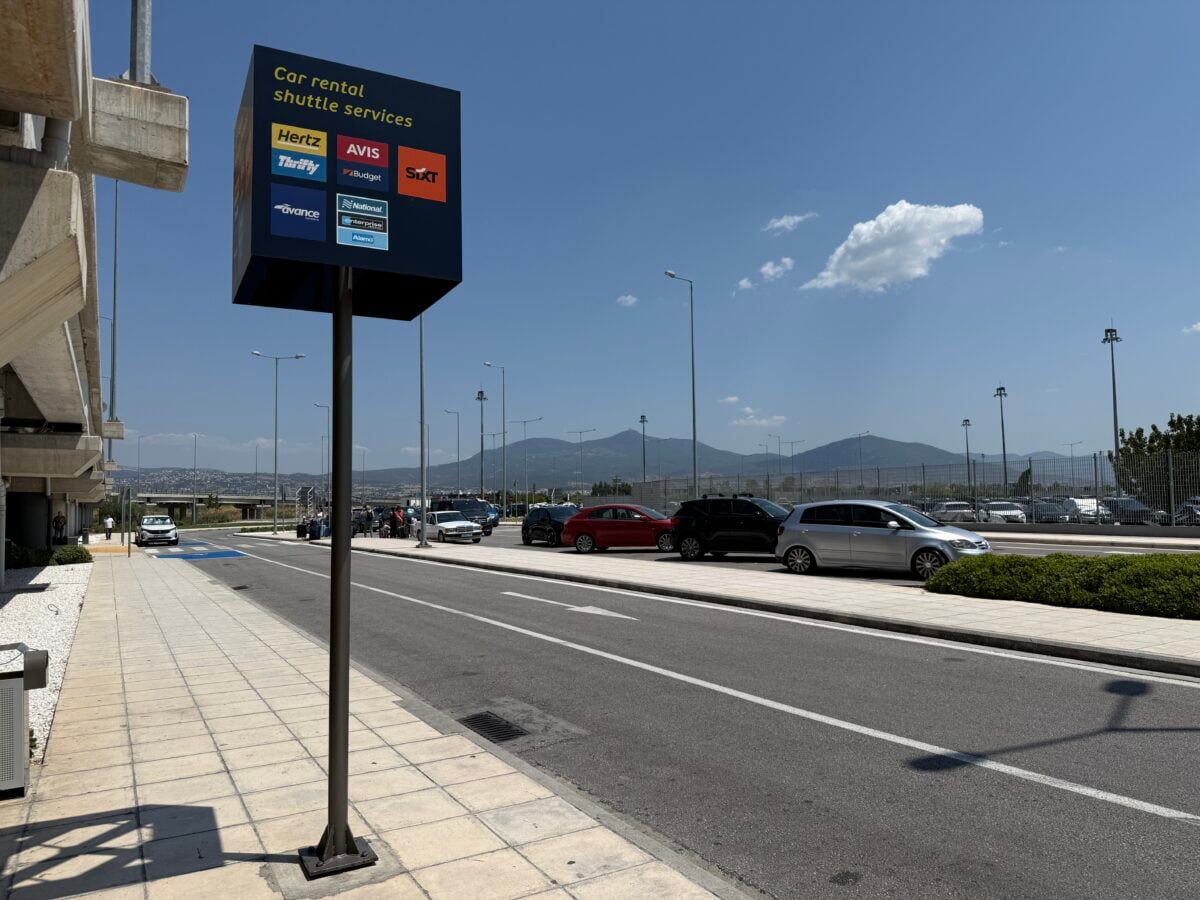 Car rental shuttle services sign outside Terminal 2 at Thessaloniki Airport showing the shuttle pick-up point for major car hire companies.