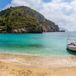 Small boat anchored in the crystal-clear waters of Paleokastritsa Beach in Corfu, Greece.