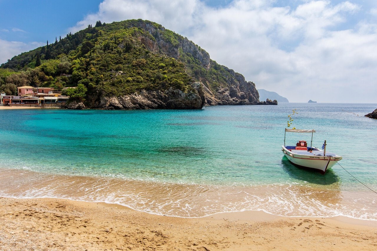 Small boat anchored in the crystal-clear waters of Paleokastritsa Beach in Corfu, Greece.