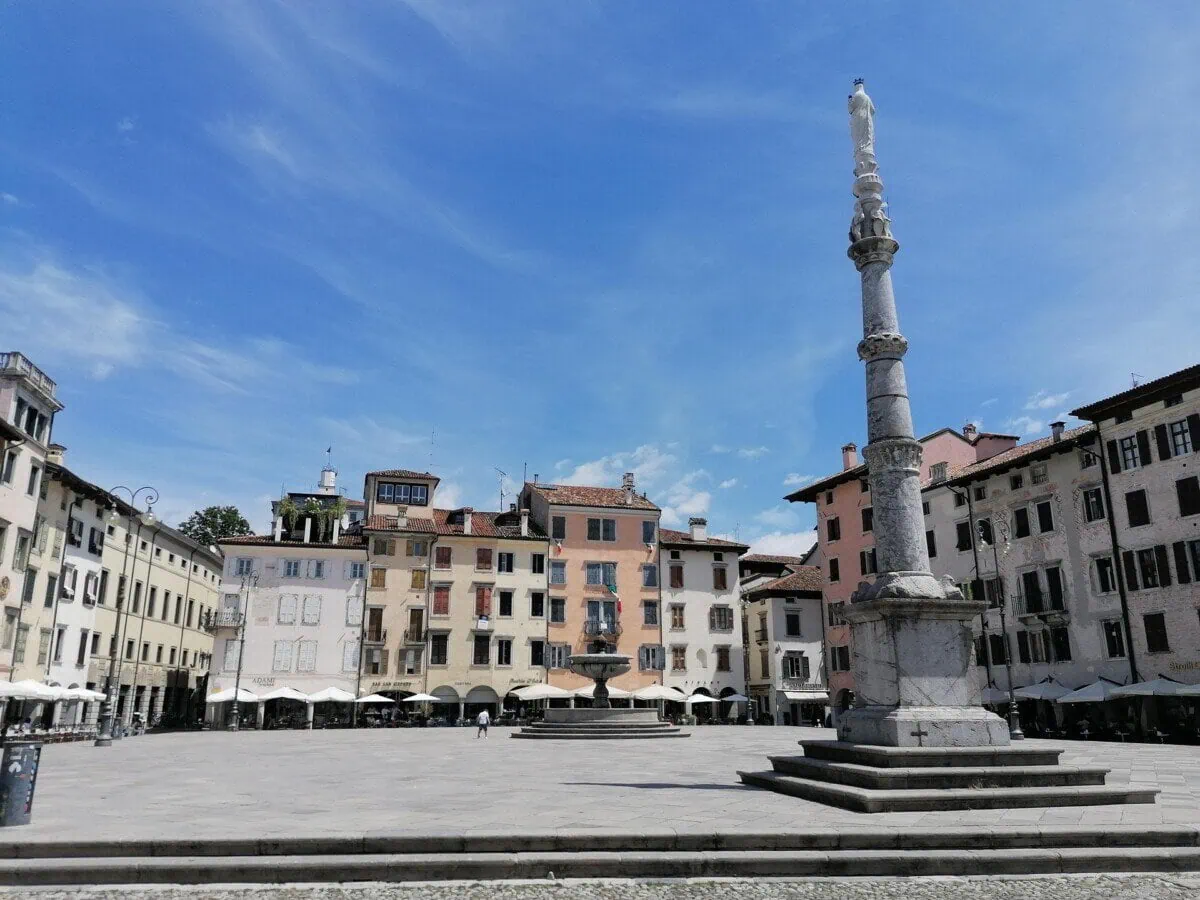 Historic square in Udine with a stone column and colourful Italian buildings