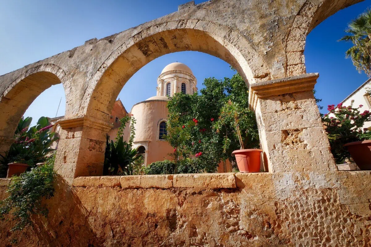 Historic stone monastery courtyard with arches and a domed church in Crete