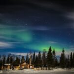 Northern Lights over snowy cabins and forest near Kiruna, Swedish Lapland
