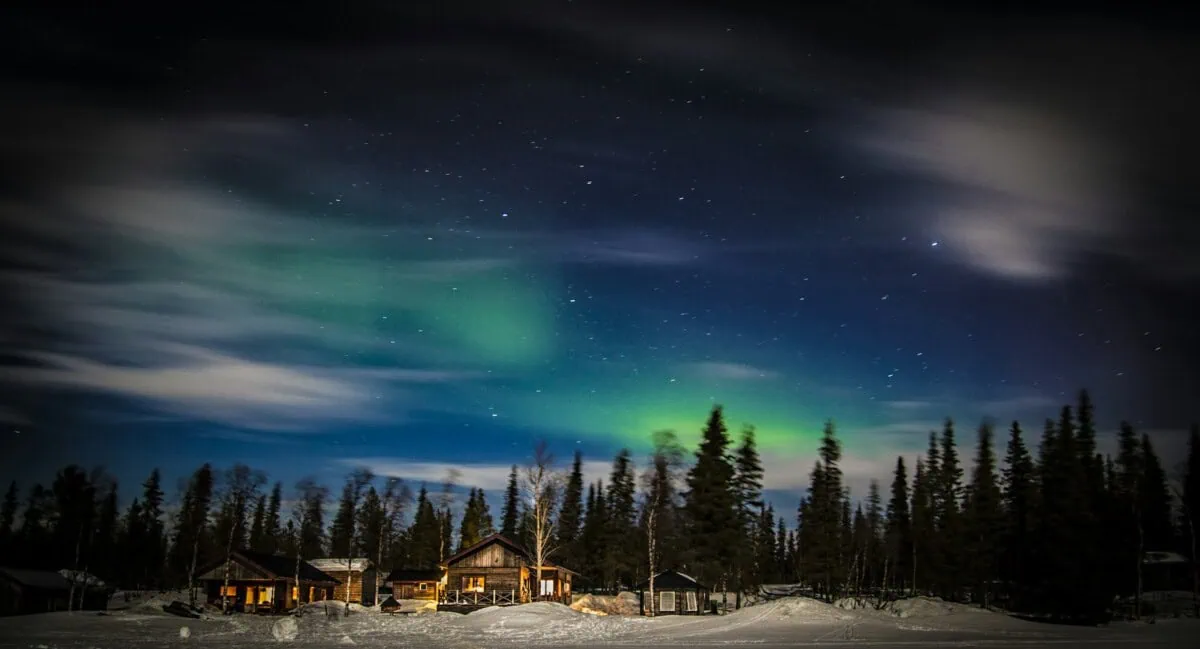 Northern Lights over snowy cabins and forest near Kiruna, Swedish Lapland