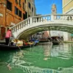 Gondolas passing beneath a stone bridge on a Venice canal