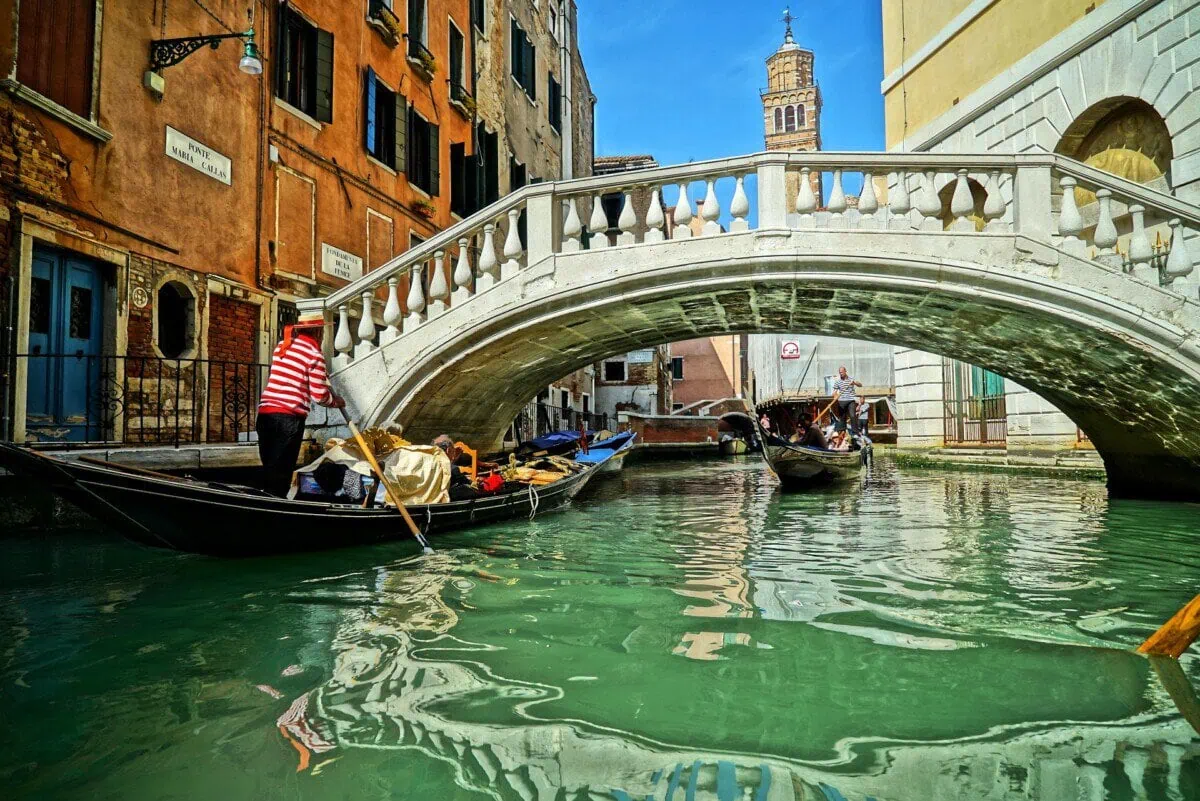 Gondolas passing beneath a stone bridge on a Venice canal