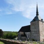 Historic stone church with a tall spire and graveyard in the Åland Islands