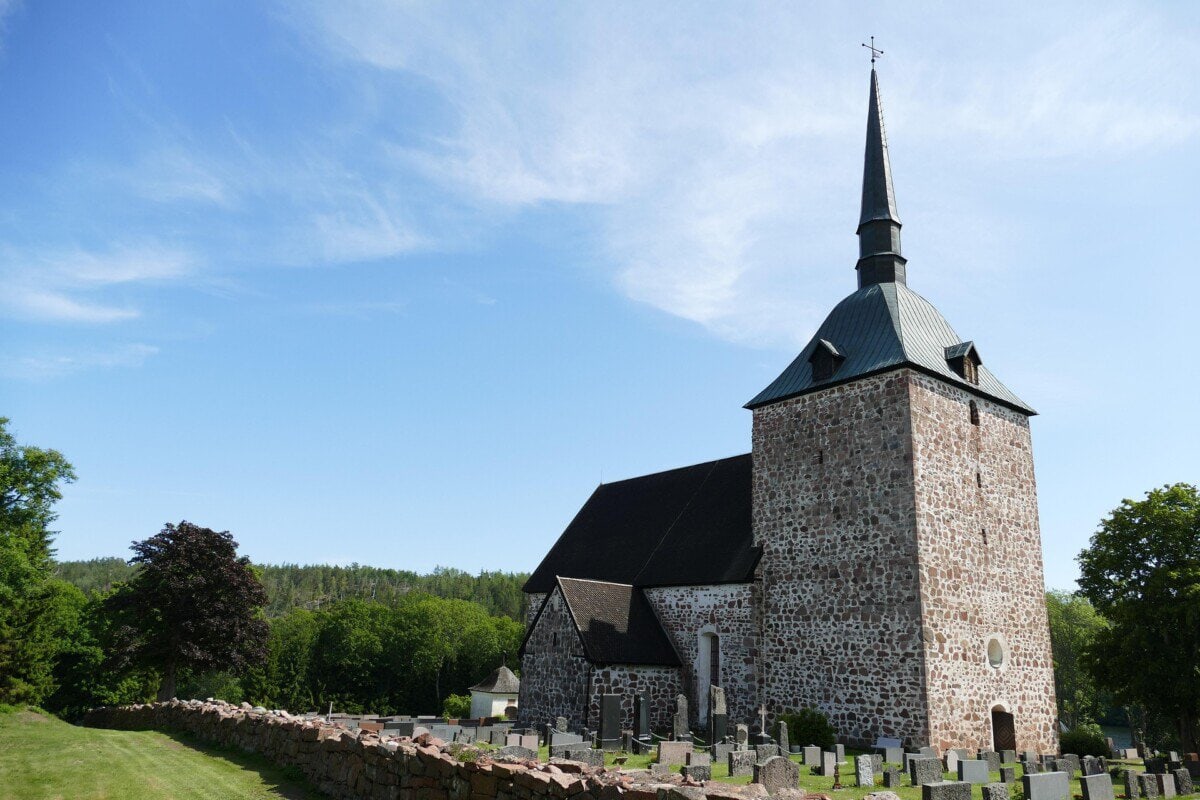 Historic stone church with a tall spire and graveyard in the Åland Islands