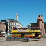 Riga Old Town with a sightseeing bus and the Latvian Riflemen Monument under a clear blue sky