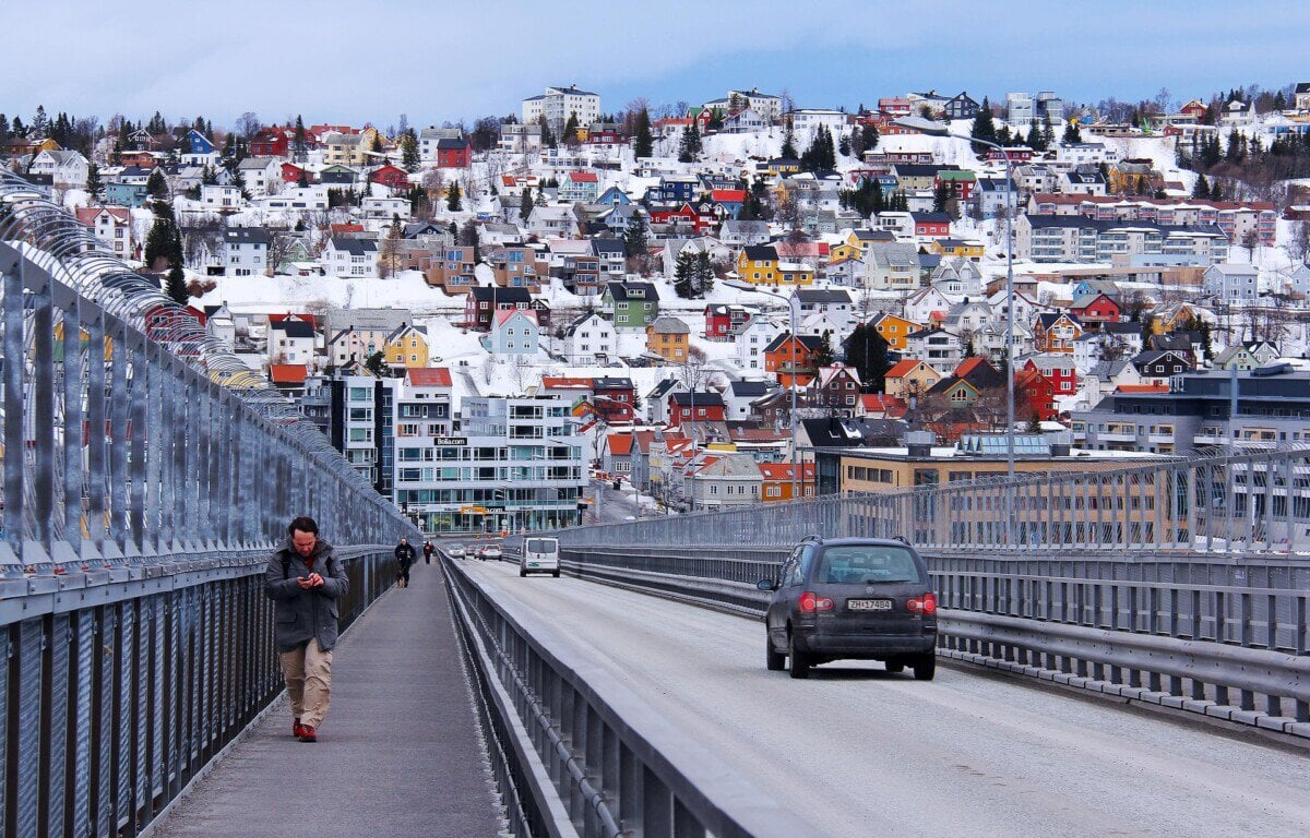 Road crossing a bridge into snowy Tromsø with colourful hillside houses beyond