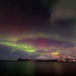 Northern lights glowing over snowy mountains and water near Tromsø in northern Norway