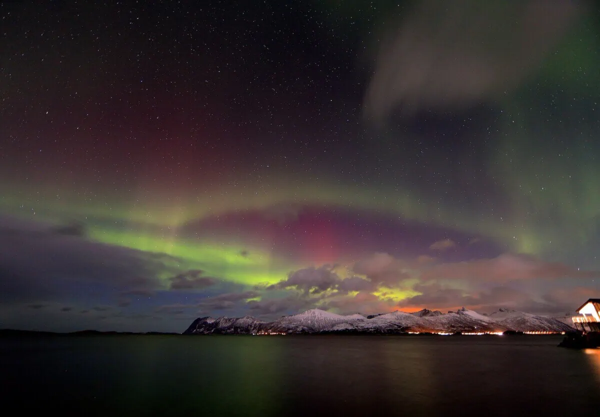 Northern lights glowing over snowy mountains and water near Tromsø in northern Norway