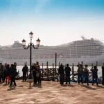 Large cruise ship sailing near Venice with waterfront crowds